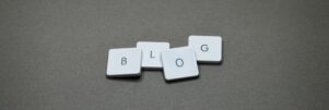 White Scrabble tiles spelling 'Blog' against a minimalist gray background.
